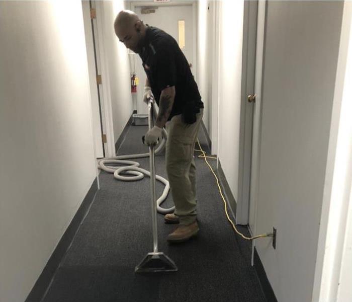 Technician using a vacuum extractor on a soaked carpet floor.